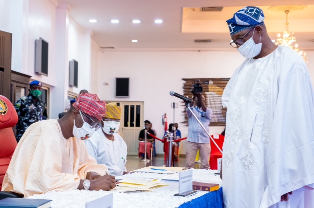 L-R: Lagos State Governor, Mr. Babajide Sanwo-Olu (left), signing the Oath of Allegiance of Mr. David Famuyiwa as the new Chairman of Agbado-Oke Odo LCDA (right), while the Commissioner for Local Government and Community Affairs, Dr. Wale Ahmed (second left), watches, during the swearing-in of the new Chairman of Agbado-Oke Odo LCDA, at Lagos House, Alausa, Ikeja, on Tuesday, June 30, 2020.
